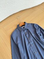 Camicia blu elegante su gruccia di legno in ambiente raffinato e luminoso.