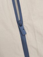 Cerniera blu contrastante su tessuto beige, dettaglio di stile e qualità.