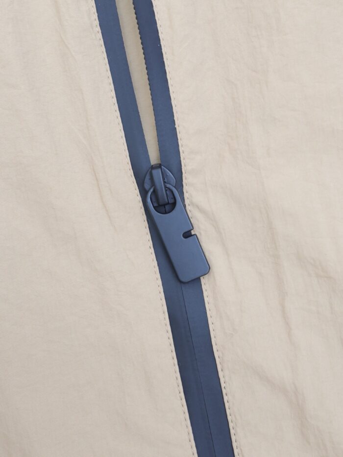 Cerniera blu contrastante su tessuto beige, dettaglio di stile e qualità.
