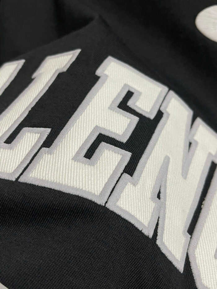 Maglietta moderna con scritta Eccellenza bianca su sfondo nero, stile streetwear di tendenza.