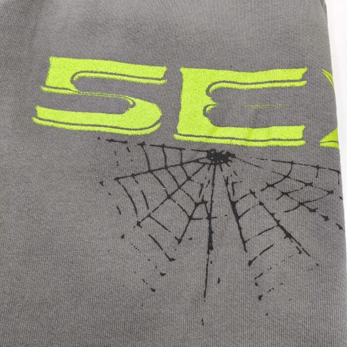 T-shirt grigia con scritta SEX gialla e ragnatela nera, stile urbano e audace.