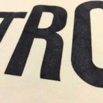 Tessuto casual con grandi lettere nere su tessuto di cotone chiaro, stile streetwear moderno.