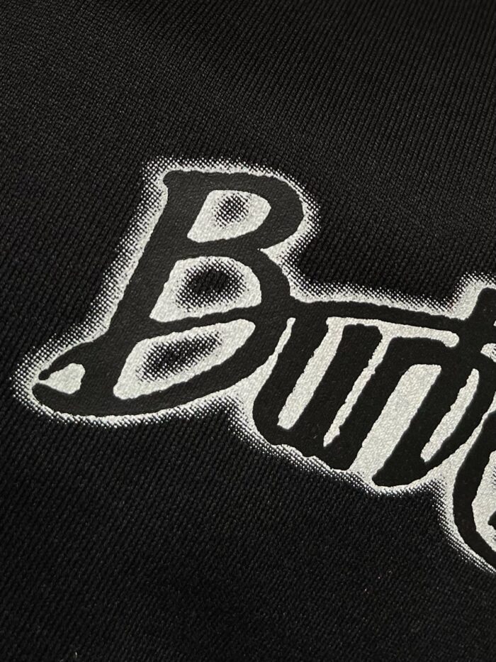 Lettere Butter in stile grafico su tessuto nero, perfette per streetwear alla moda.