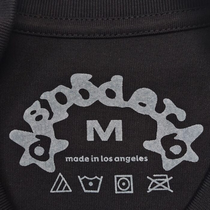 Etichetta sp0der con logo, taglia M, simboli di cura su sfondo nero.