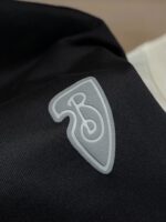 Dettaglio di logo stilizzato su tessuto nero elegante con contrasto e design moderno.