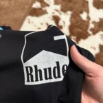 Maglietta nera Rhude con logo bold e dettaglio animalier sullo sfondo.