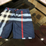 Shorts da spiaggia blu navy con fantasia a quadri e fascia rossa, estilo estivo e moderno.
