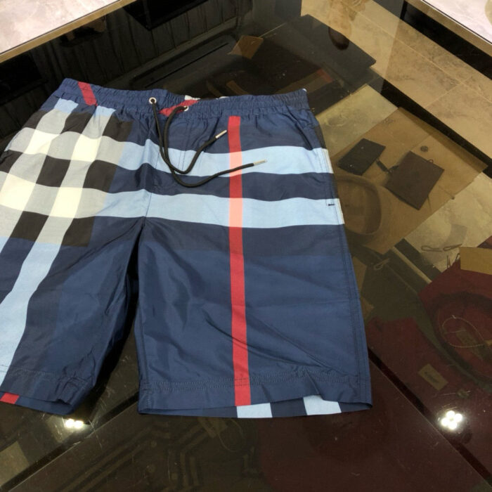 Shorts da spiaggia blu navy con fantasia a quadri e fascia rossa, estilo estivo e moderno.