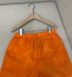 Pantaloncini arancioni casual in nylon con cintura elastica, appesi su gruccia di legno.