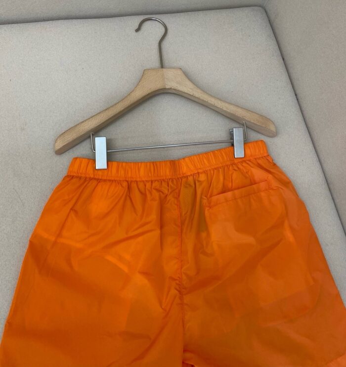 Pantaloncini arancioni casual in nylon con cintura elastica, appesi su gruccia di legno.