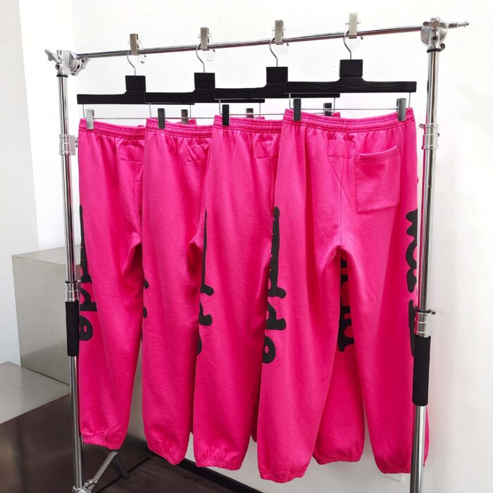 Pantaloni sportivi rosa fluorescente con lettere nere, stile streetwear su rack moderno.