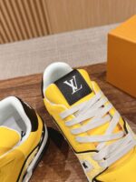Sneakers Louis Vuitton gialle e nere con logo “LV”, su tavolo di legno, stile sportivo.