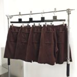 Shorts marroni in esposizione minimalista, tessuto morbido con tasche laterali, ambiente moderno e luminoso.