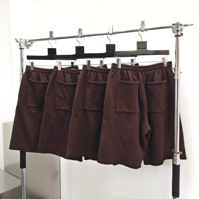 Shorts marroni in esposizione minimalista, tessuto morbido con tasche laterali, ambiente moderno e luminoso.