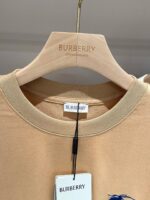 Camicia beige Burberry con ricamo logo, design elegante e dettagli di lusso su gancio di legno.