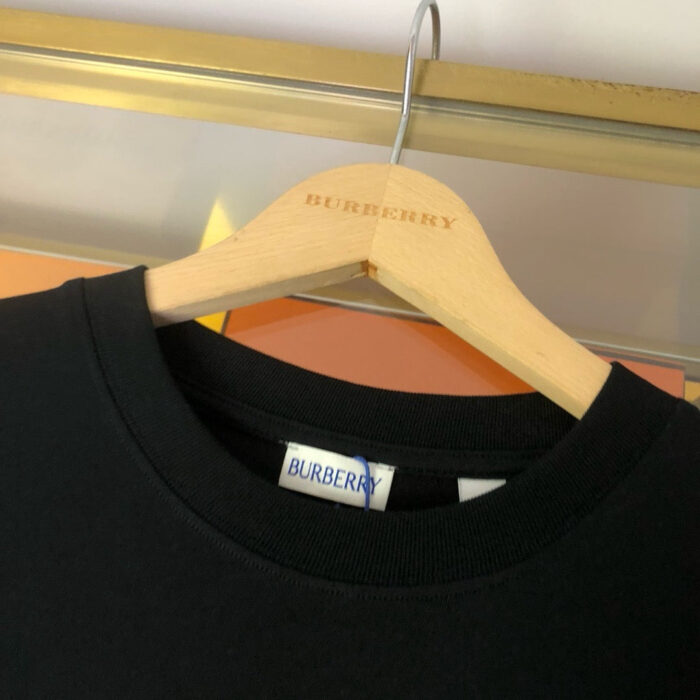 Maglietta nera Burberry con etichetta, appesa su appendiabiti in legno elegante.