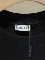 Maglione nero Burberry con etichetta brand sul colletto, su supporto in legno elegante.