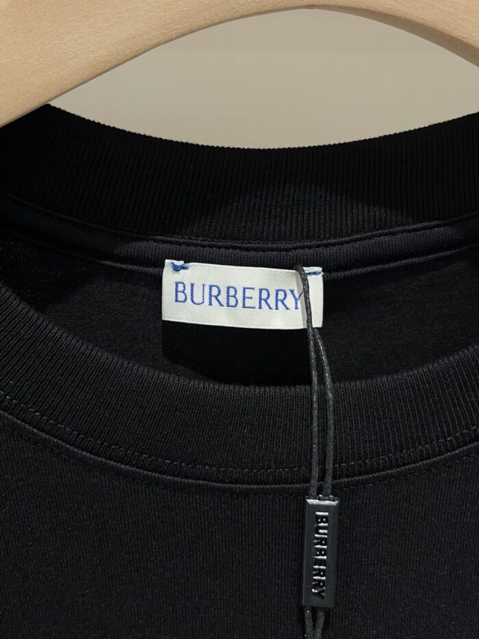 Maglione nero Burberry con etichetta brand sul colletto, su supporto in legno elegante.