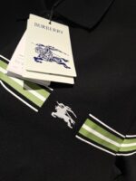 Polo Burberry nera con strisce verdi e logo iconico, stile elegante e moderno.