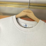 Maglione Burberry crema su appendiabiti di legno elegante, stile luxury e design raffinato.