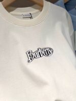 Felpa Burberry crema con logo ricamato nero, stile casual e elegante.