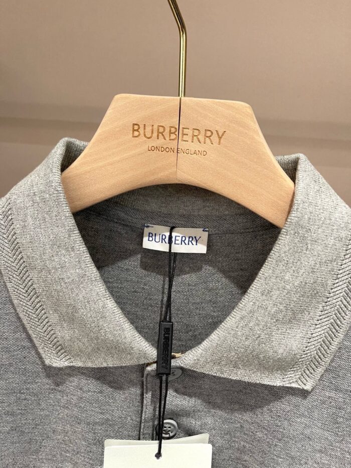 Camicia polo grigia Burberry su appendiabiti di lusso in boutique elegante.
