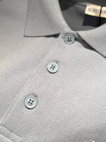 Polo Burberry grigia in cotone di lusso con bottoni azzurri e dettagli eleganti.