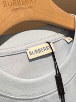 Camicia Burberry blu pastello su cavalletto in legno, logo elegante e dettagli di lusso.