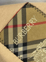 Dettaglio di logo Ricamato Burberry su tessuto di lusso con motivo check classico.
