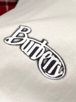 Logo Burberry in nero con bordo bianco su tessuto di lusso, simbolo di eleganza e raffinatezza.