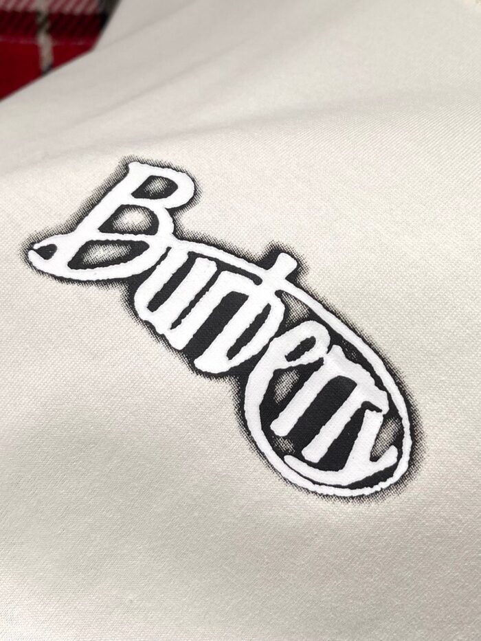 Logo Burberry in nero con bordo bianco su tessuto di lusso, simbolo di eleganza e raffinatezza.