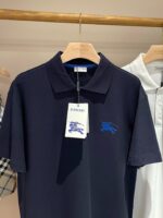 Maglietta polo Burberry blu navy, elegante, con logo ricamato, su appendiabiti in legno.