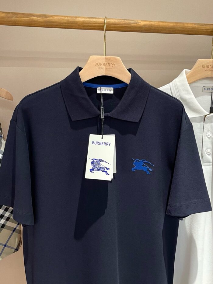 Maglietta polo Burberry blu navy, elegante, con logo ricamato, su appendiabiti in legno.