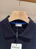 Camicia polo navy Burberry su appendiabiti in legno con logo inciso, stile elegante e di lusso.