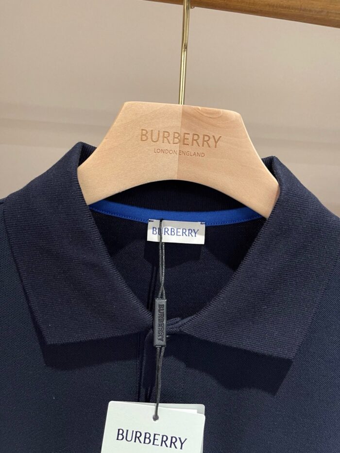 Camicia polo navy Burberry su appendiabiti in legno con logo inciso, stile elegante e di lusso.