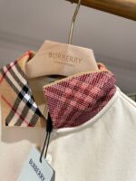 Polo Burberry con collo doppio pattern check e rosso, su gruccia di legno elegante.