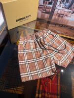 Pantaloncini Burberry quadri marroni, stile casual di lusso, con scatola elegante in sfondo.