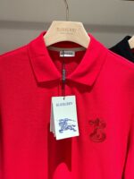 Polo rossa Burberry con logo ricamato e etichetta elegante su appendiabiti in legno.