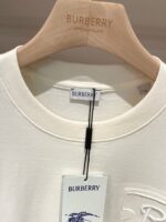 Maglietta Burberry bianca minimalista con etichetta e attaccapanni in legno elegante.