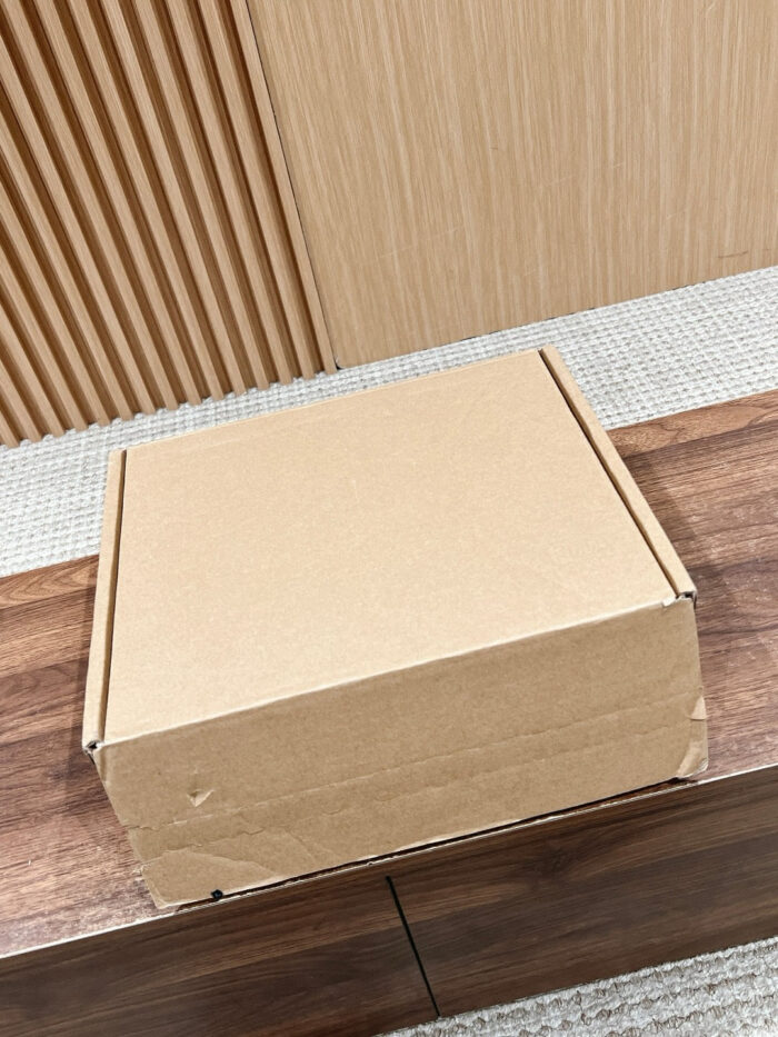 Scatola di cartone semplice su superficie in legno raffinato, luce soffusa e parete a greche.