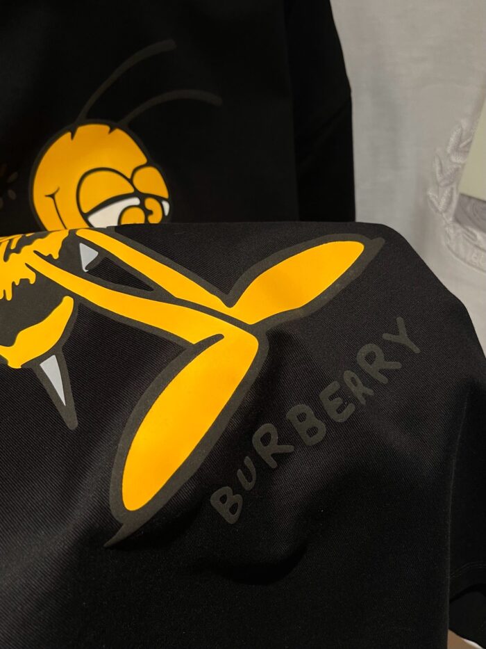 Logo Burberry con ape cartoon colorata su tessuto nero, stile giovane e originale.
