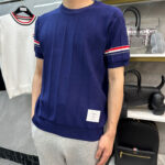 Maglione navy con strisce rosse e bianche, pantaloni grigi in stile casual sportivo.