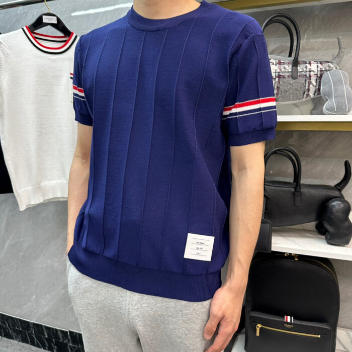 Maglione navy con strisce rosse e bianche, pantaloni grigi in stile casual sportivo.