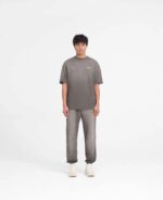 Uomo giovane in stile casual athleisure con t-shirt grigia, jogger e sneakers chiare.