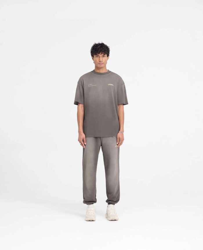 Uomo giovane in stile casual athleisure con t-shirt grigia, jogger e sneakers chiare.