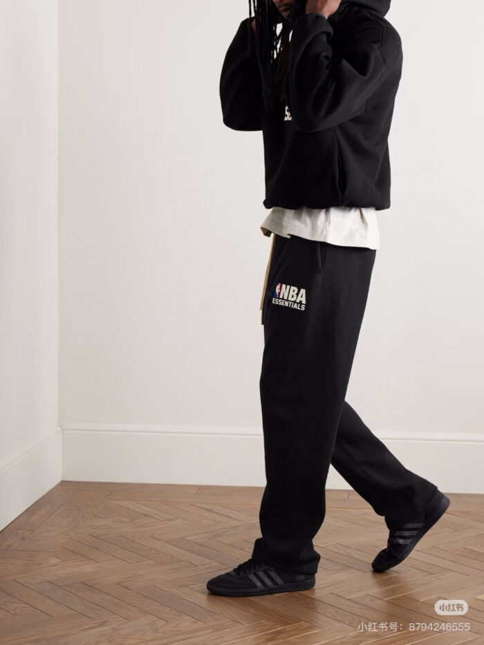 Stile streetwear casual con felpa NBA, pantaloni larghi e sneakers nere in ambienti moderni.