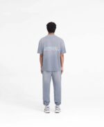 Persona da dietro in outfit sportivo casual grigio con sneakers moderni su sfondo minimalista.