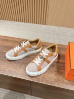 Sneakers beige e arancio moderne, comode e stile urbano su superficie in legno con packaging vibrante.