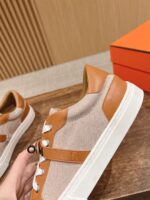 Sneakers beige in tessuto e pelle tan con dettagli moderni, su superficie in legno naturale.