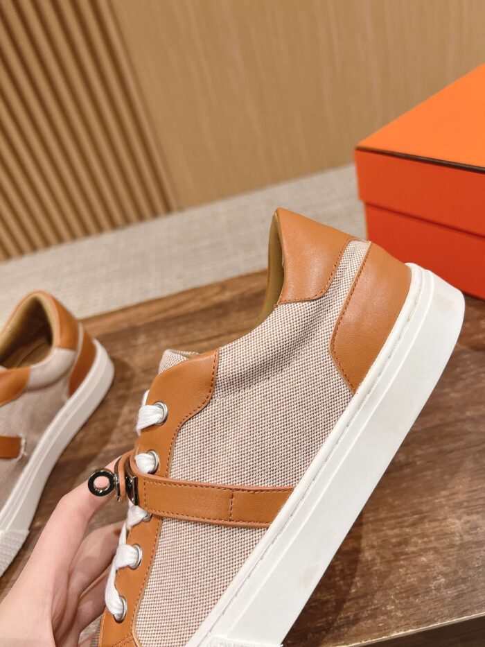 Sneakers beige in tessuto e pelle tan con dettagli moderni, su superficie in legno naturale.